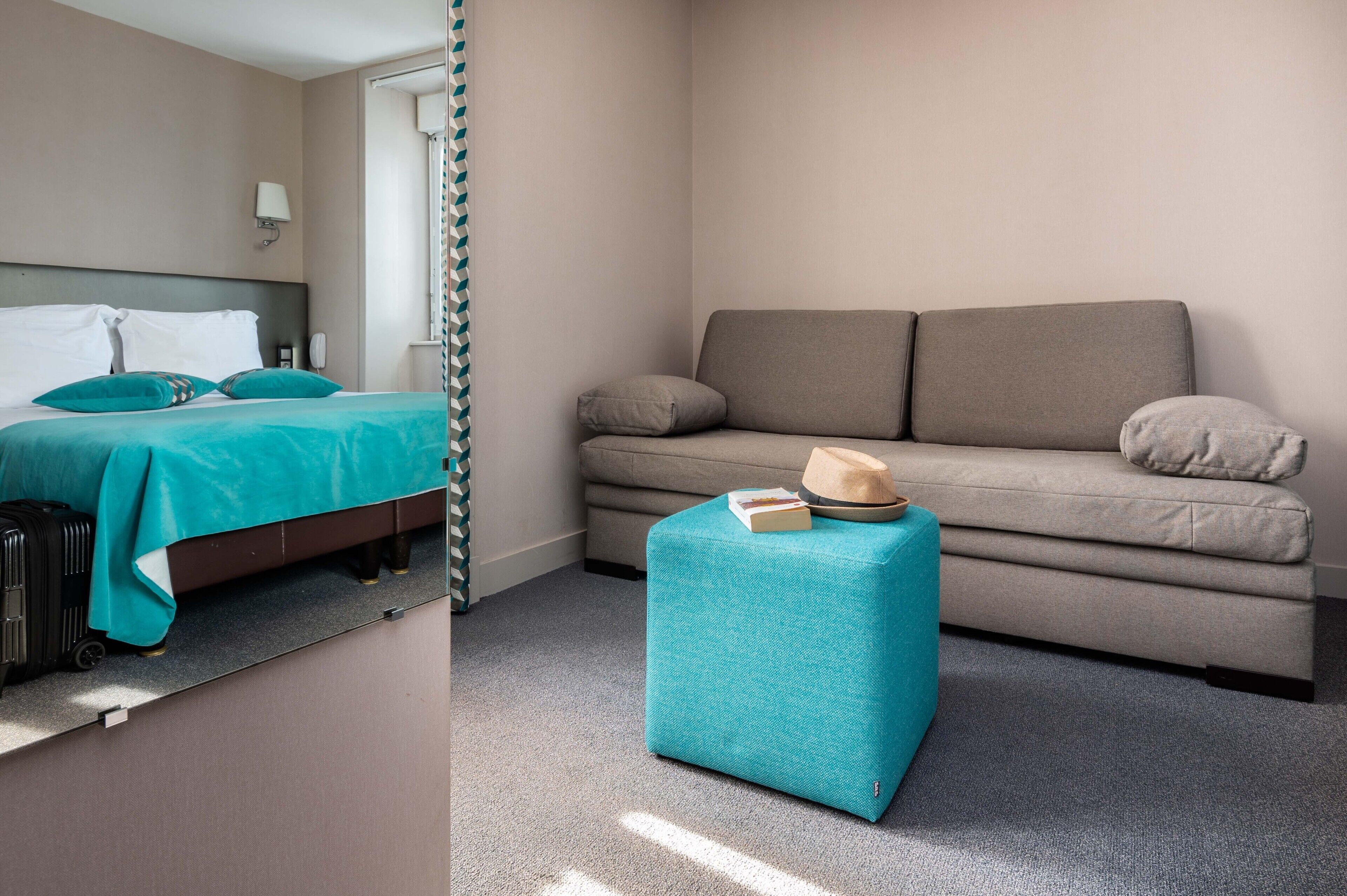 A hotel room with a bed, a sofa, a small ottoman, and a suitcase.