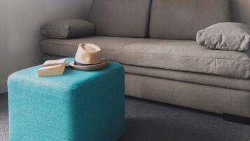 A modern living room with a grey sofa, a teal ottoman, a hat, and a book.