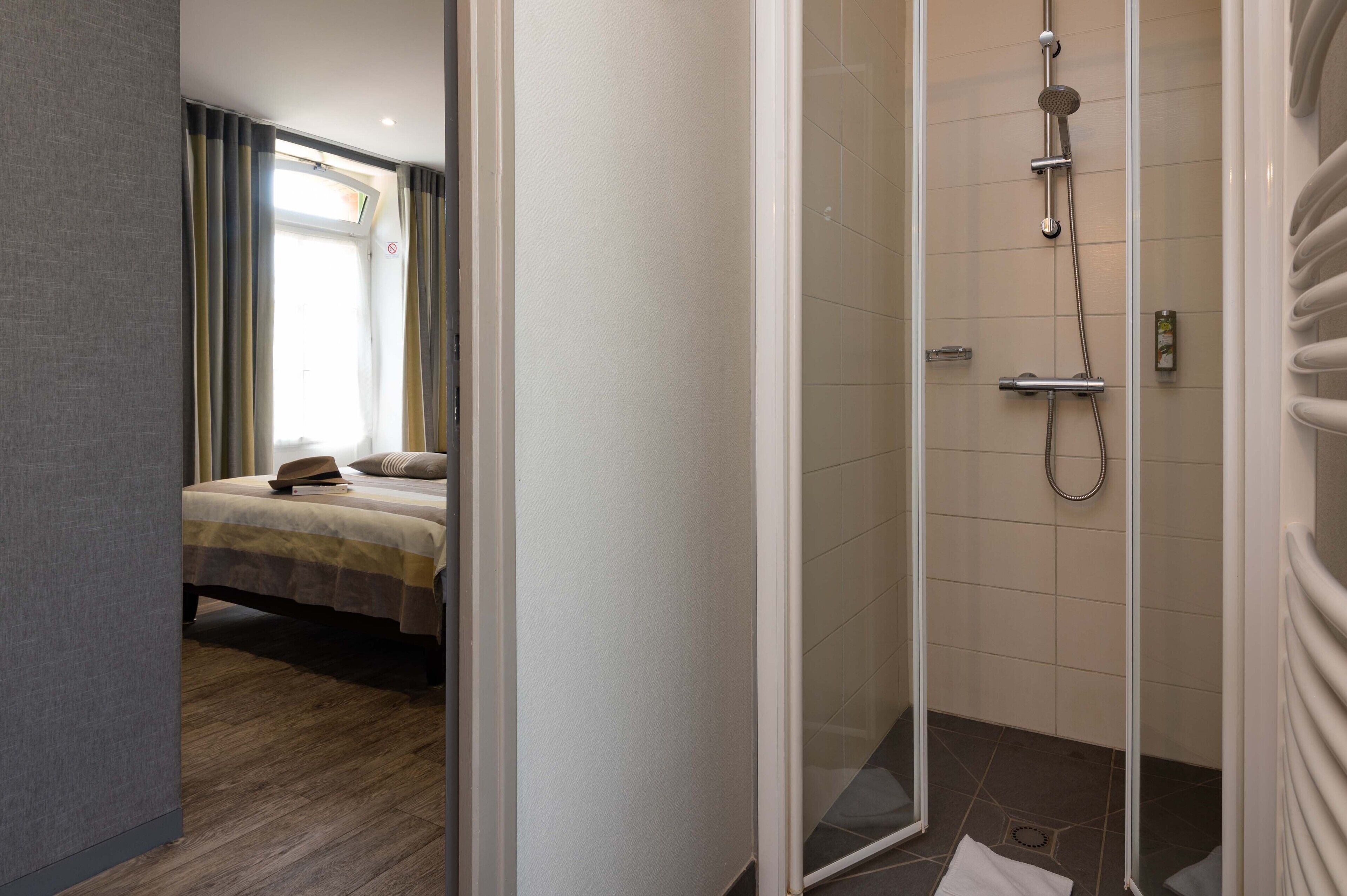 Una camera d'albergo con un letto, un angolo doccia con porta in vetro e vista all'esterno attraverso una finestra.