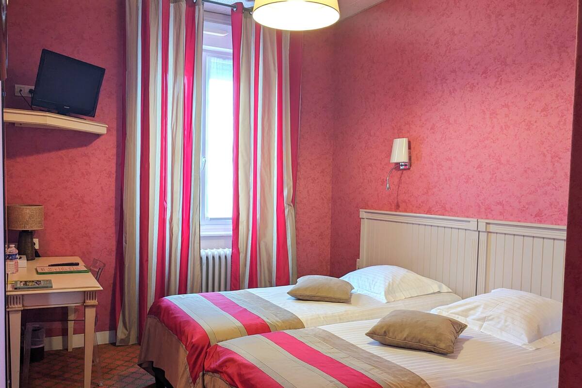 Hotellihuone, jossa on kaksi sänkyä, työpöytä, televisio ja ikkuna, jossa on verhot.