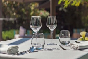 Una mesa dispuesta con tres copas de vino y una servilleta doblada, con un fondo desenfocado al aire libre.