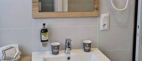 Un baño con un espejo grande, un secador de pelo, un lavabo y dos tazas sobre la encimera.