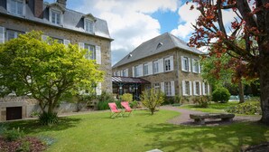 Une cour avec un bâtiment en pierre, un petit arbre et deux chaises rouges.
