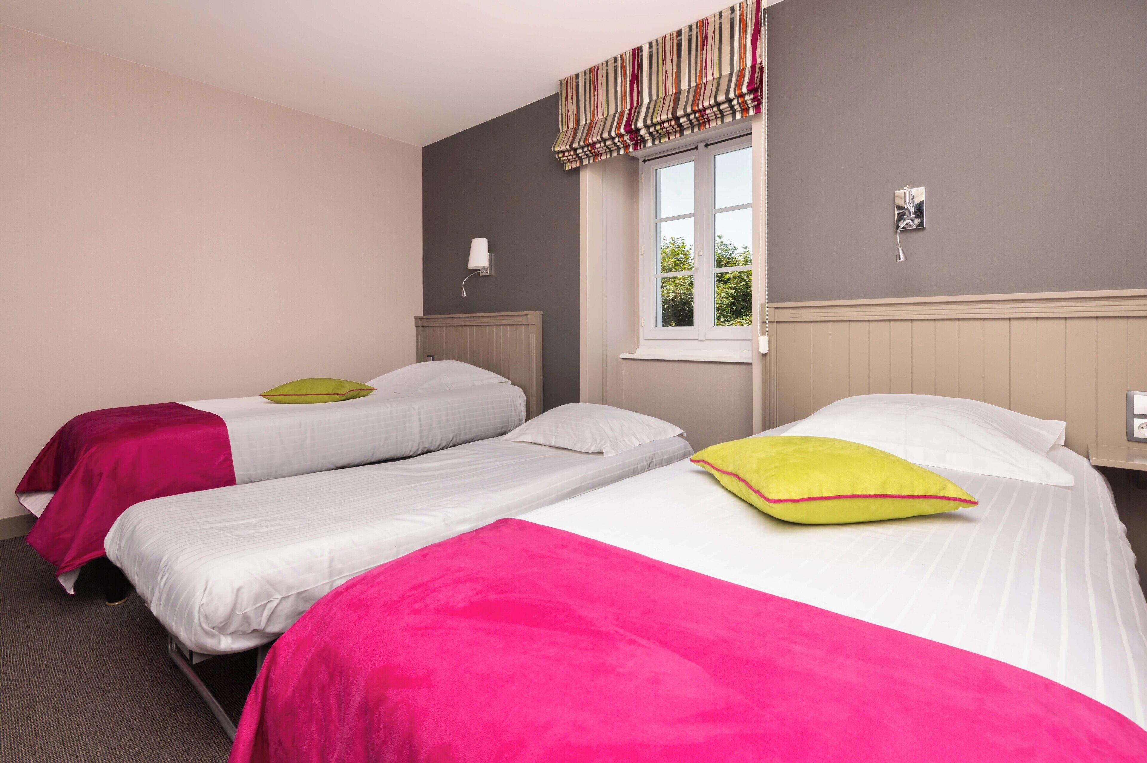 Habitación de hotel con dos camas, cada una con una colcha y almohadas de color diferente.