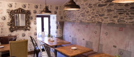 L’intérieur d’un restaurant avec des tables et des chaises en bois, des murs en pierre et des luminaires suspendus.