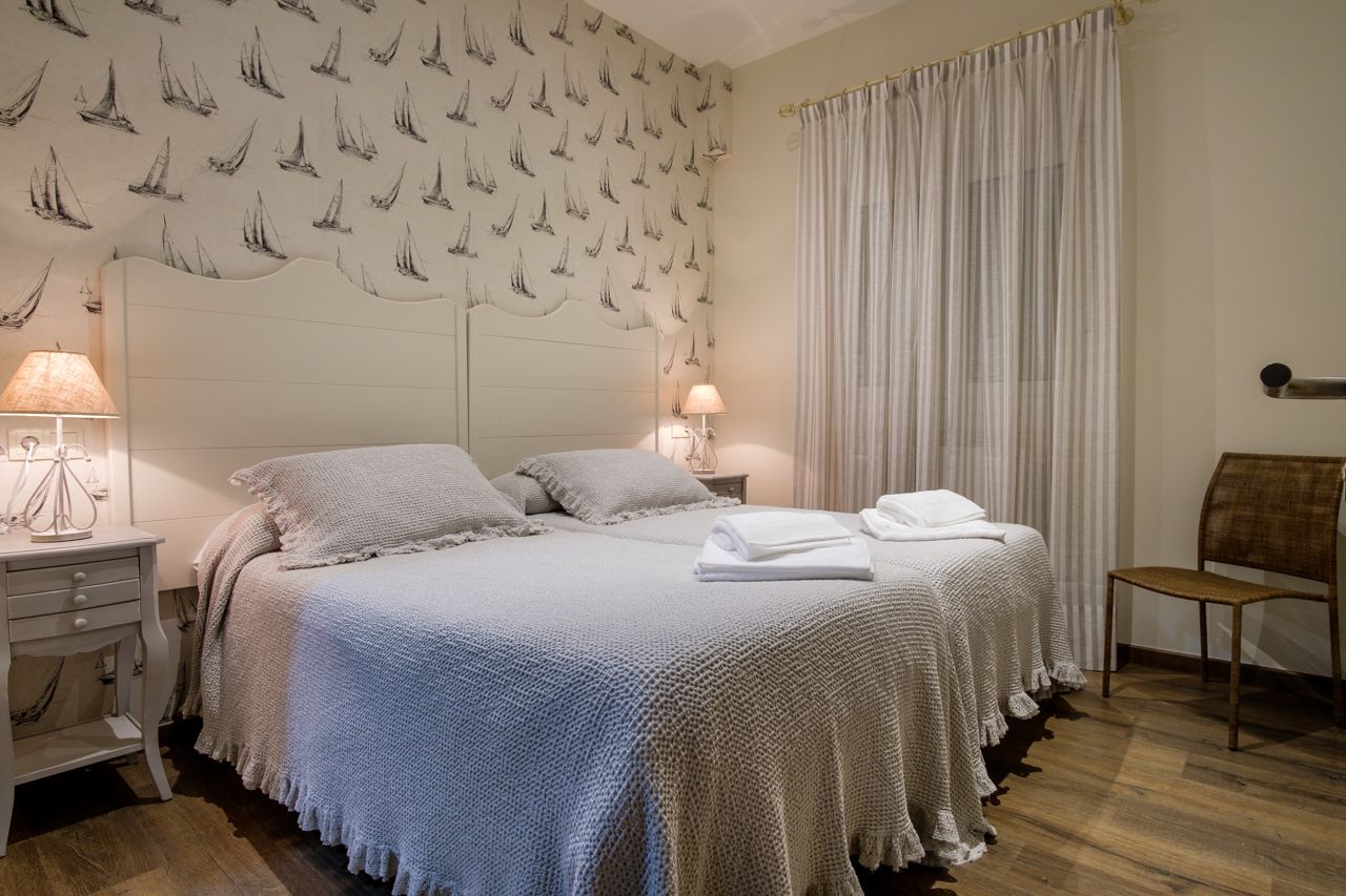 A hotel room with a large bed, two bedside tables with lamps, a chair, and a curtain.