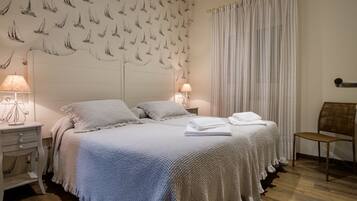 A hotel room with a large bed, two bedside tables with lamps, a chair, and a curtain.