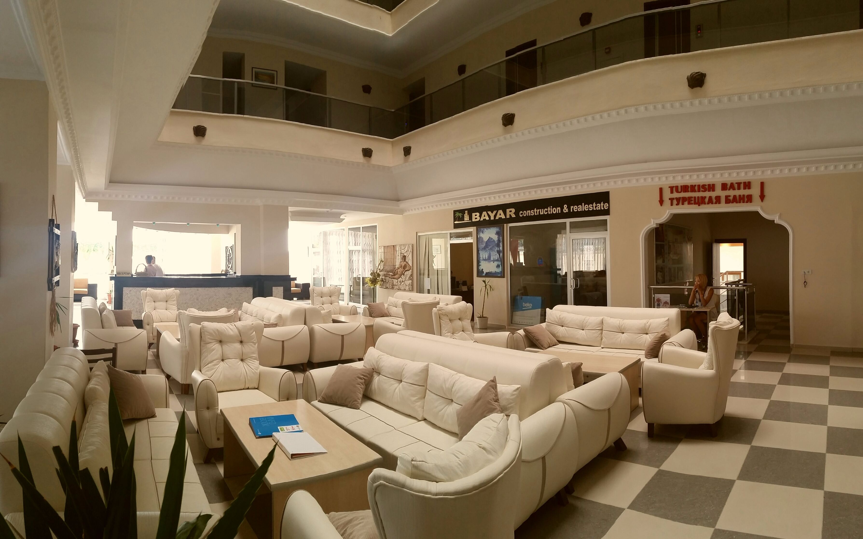 A spacious lobby with multiple seating areas, a reception desk, and a sign for 'BAYAR Construction & Real Estate'.