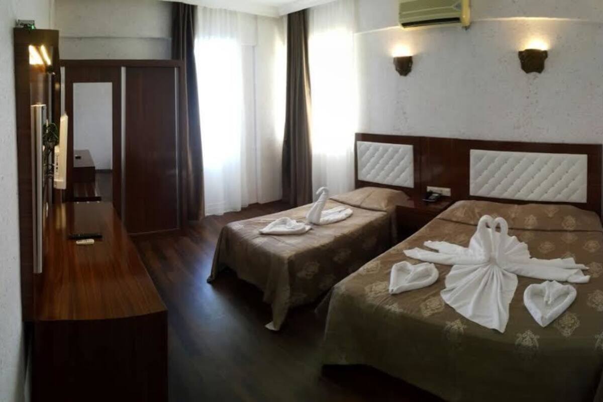 A hotel room with two beds, each with towels arranged in a swan shape. There is a wooden desk and a mirror.