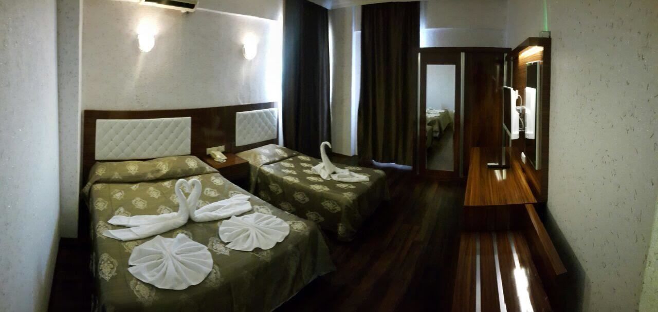 A hotel room with two beds, each with a swan towel arrangement. There is a wooden bench and a mirror.