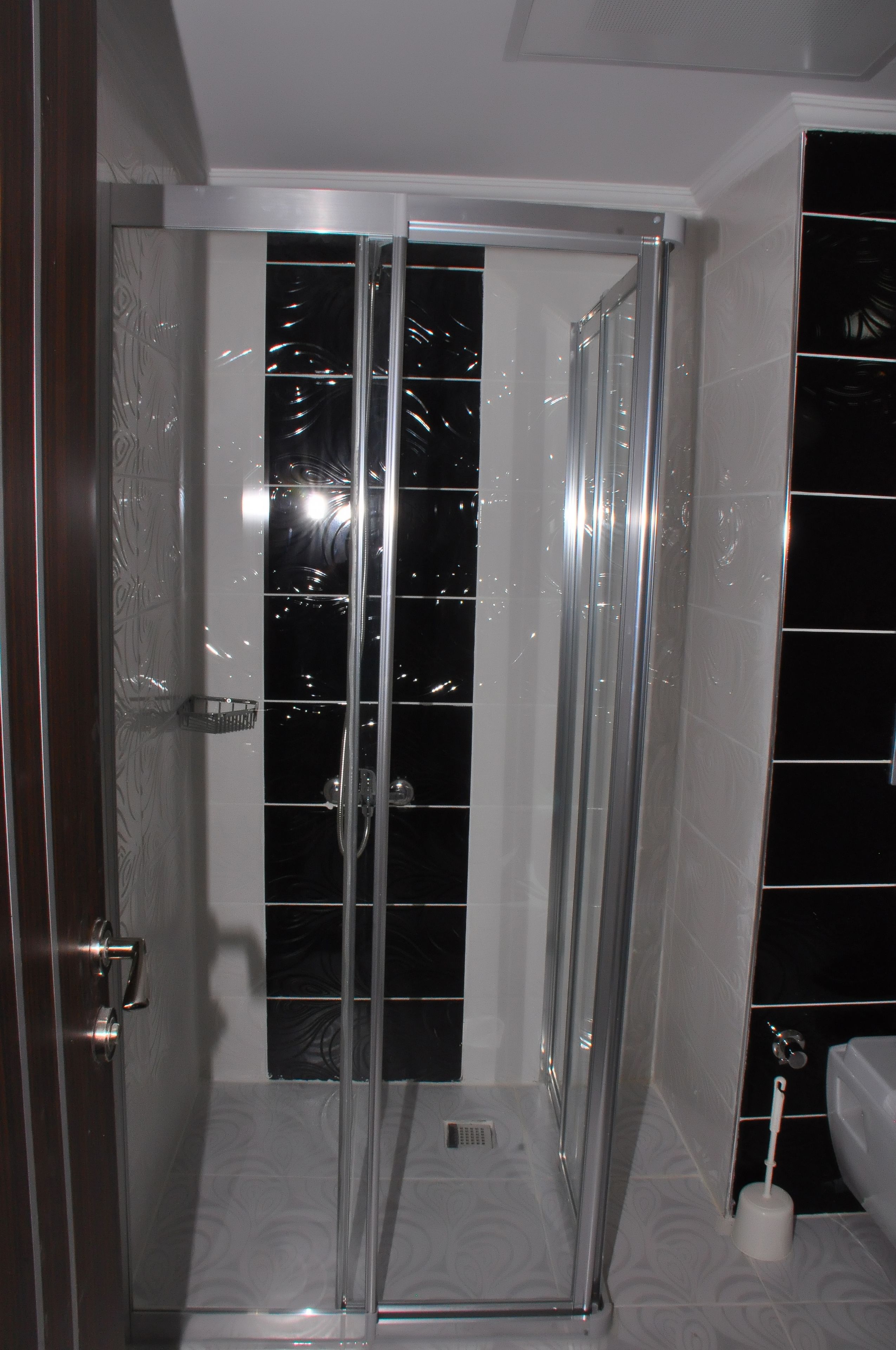 A glass-enclosed shower stall with a white tiled floor and a metal door.