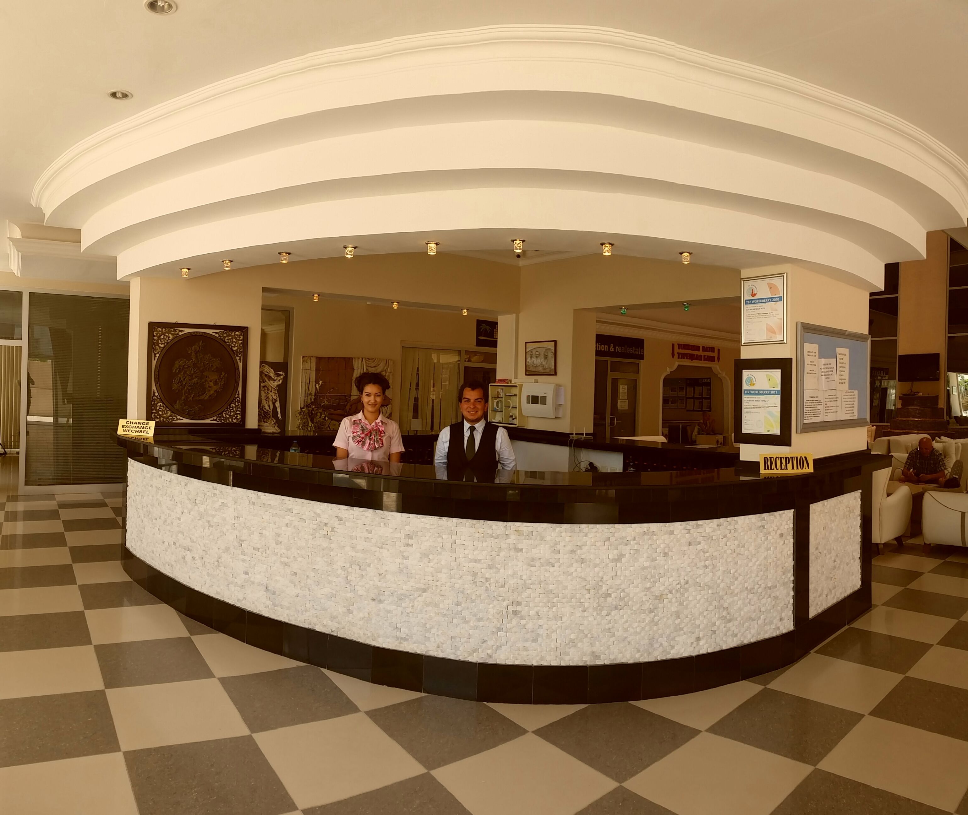En hotellobby med ett rutmönstrat golv, en receptionsdisk och en receptionist.
