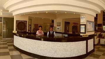 En hotellobby med ett rutmönstrat golv, en receptionsdisk och en receptionist.