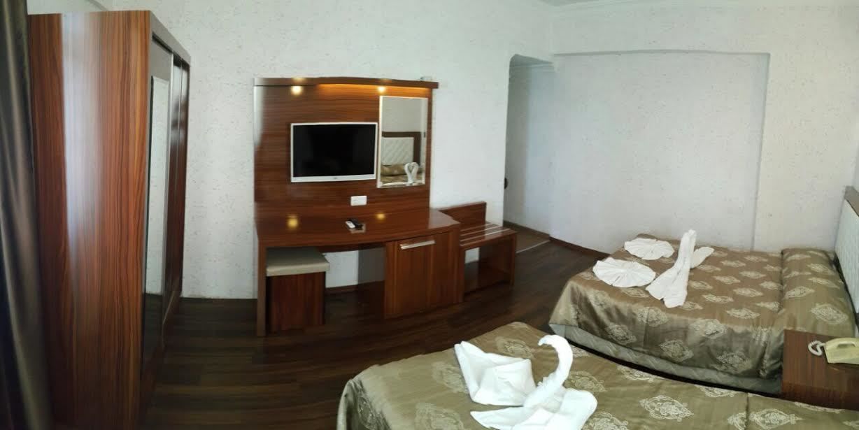Hotellihuone, jossa on puinen työpöytä, televisio, kuviollinen päiväpeite ja pyyhe sängyllä.