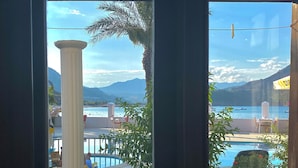 Vista a través de un ventanal de un área de piscina con un pilar blanco, sillas y una mesa.
