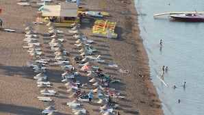 Una playa con hileras de sombrillas y sillas de baño, una torre de salvavidas y un barco en el agua.