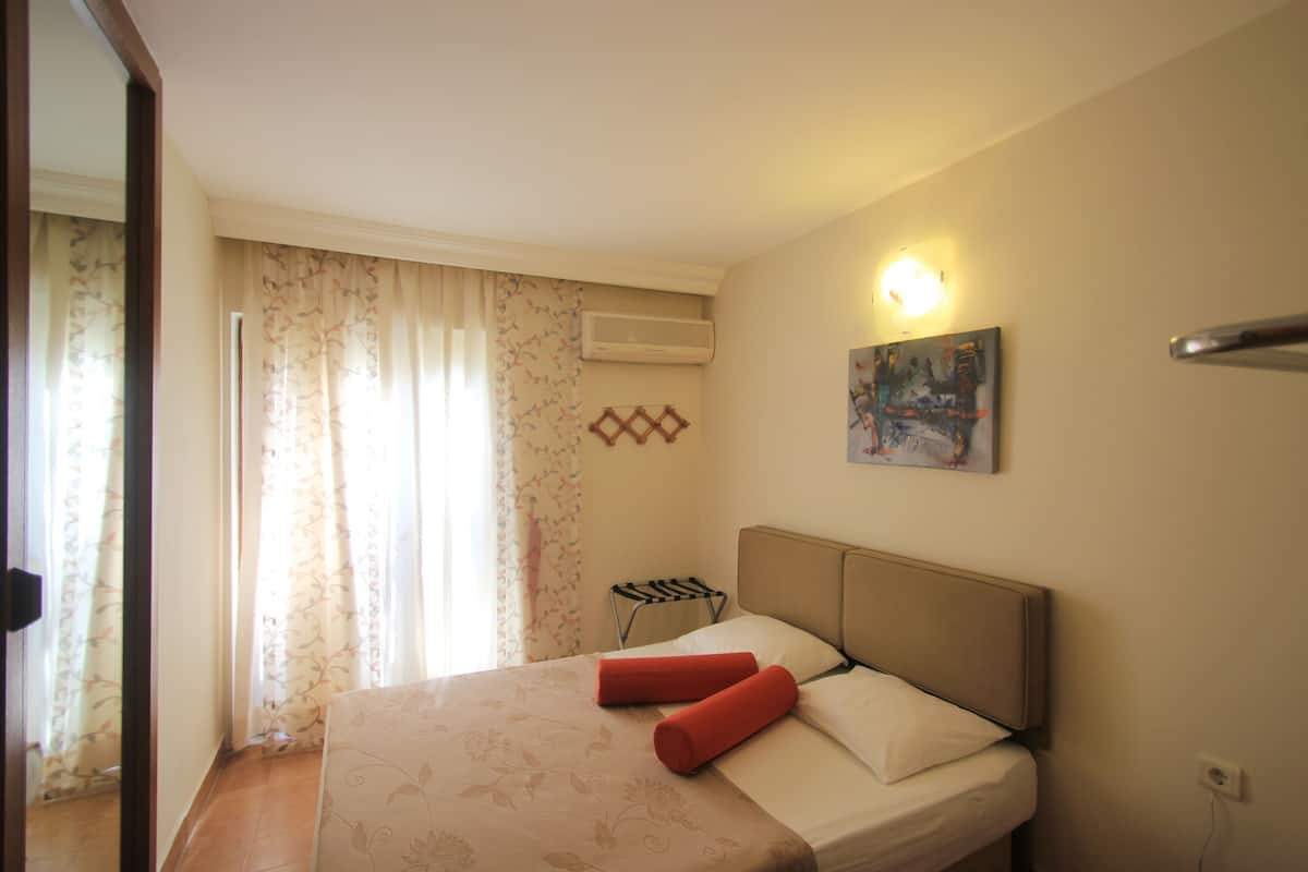 Une chambre d’hôtel avec un lit, un tableau au mur, un appareil de climatisation et une fenêtre avec des rideaux.