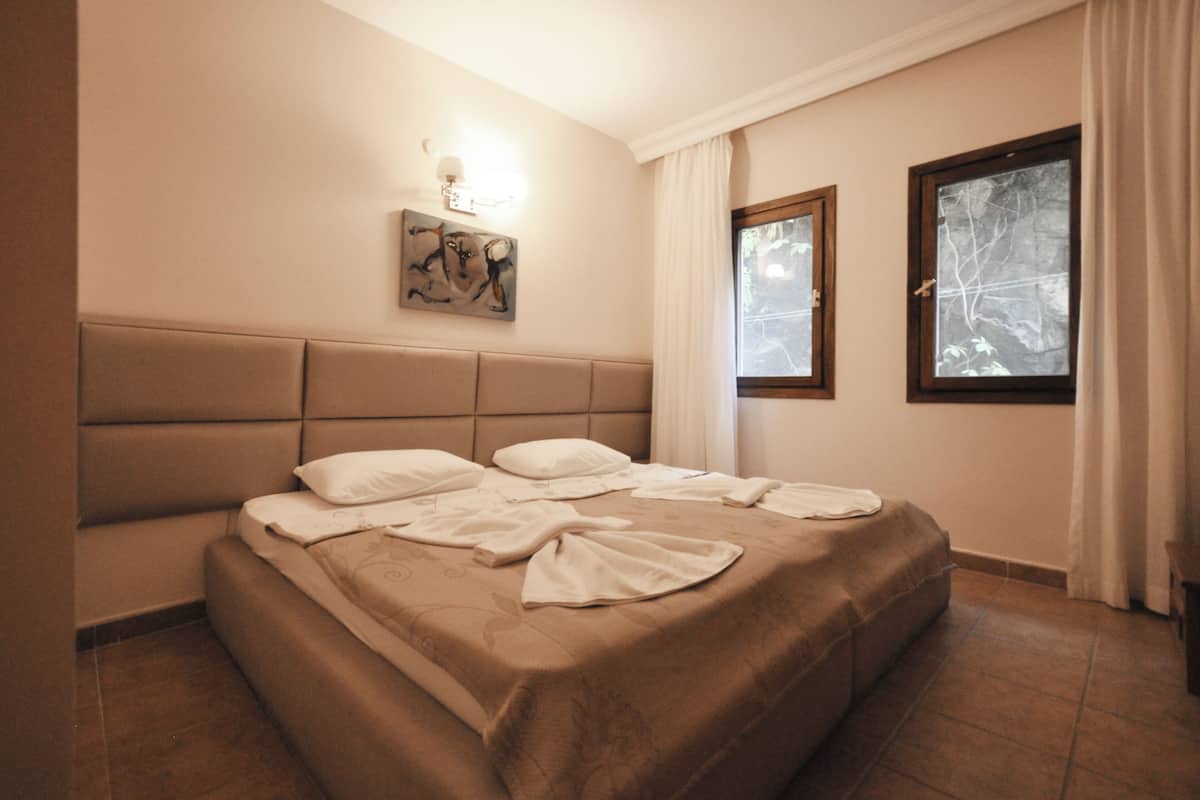 Une chambre à coucher comprenant un lit, une tête de lit, une lampe fixée au mur, une fenêtre avec des rideaux et un tableau.