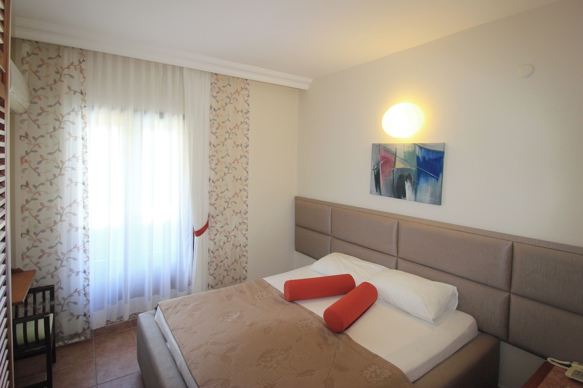 A hotel room with a bed, a chair, and a wall-mounted light.