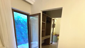 Un dormitorio con una cama grande, una banca, un armario y una puerta corrediza de vidrio que da a un balcón.