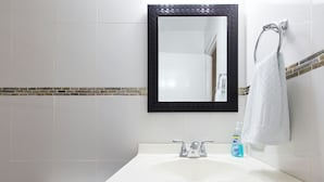 Une salle de bain avec un lavabo blanc, un miroir à cadre noir, une serviette suspendue à un porte-serviettes et un flacon de savon liquide.