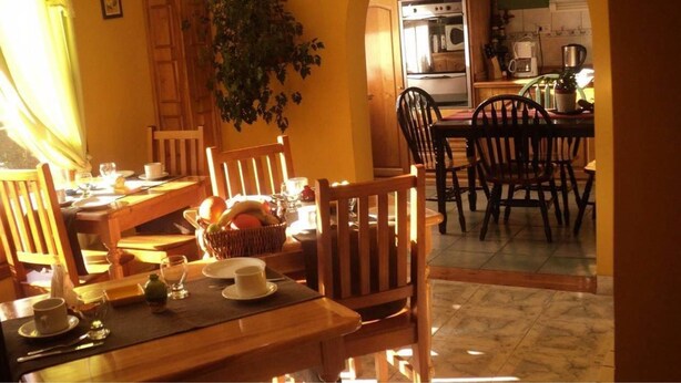 Zona pranzo con mobili in legno, cucina sullo sfondo e una pianta in vaso.