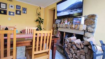 A cozy living room with a stone fireplace, a television mounted above it, and a dining area with wooden furniture.