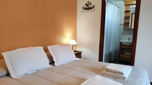 Una camera d'albergo con un letto, due cuscini, un comodino con una lampada e un bagno visibile attraverso una porta.