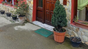 Un edificio con facciata in pietra, una porta in legno e un portico con trave di legno. Sul terreno, vasi con piante e un tappetino verde.