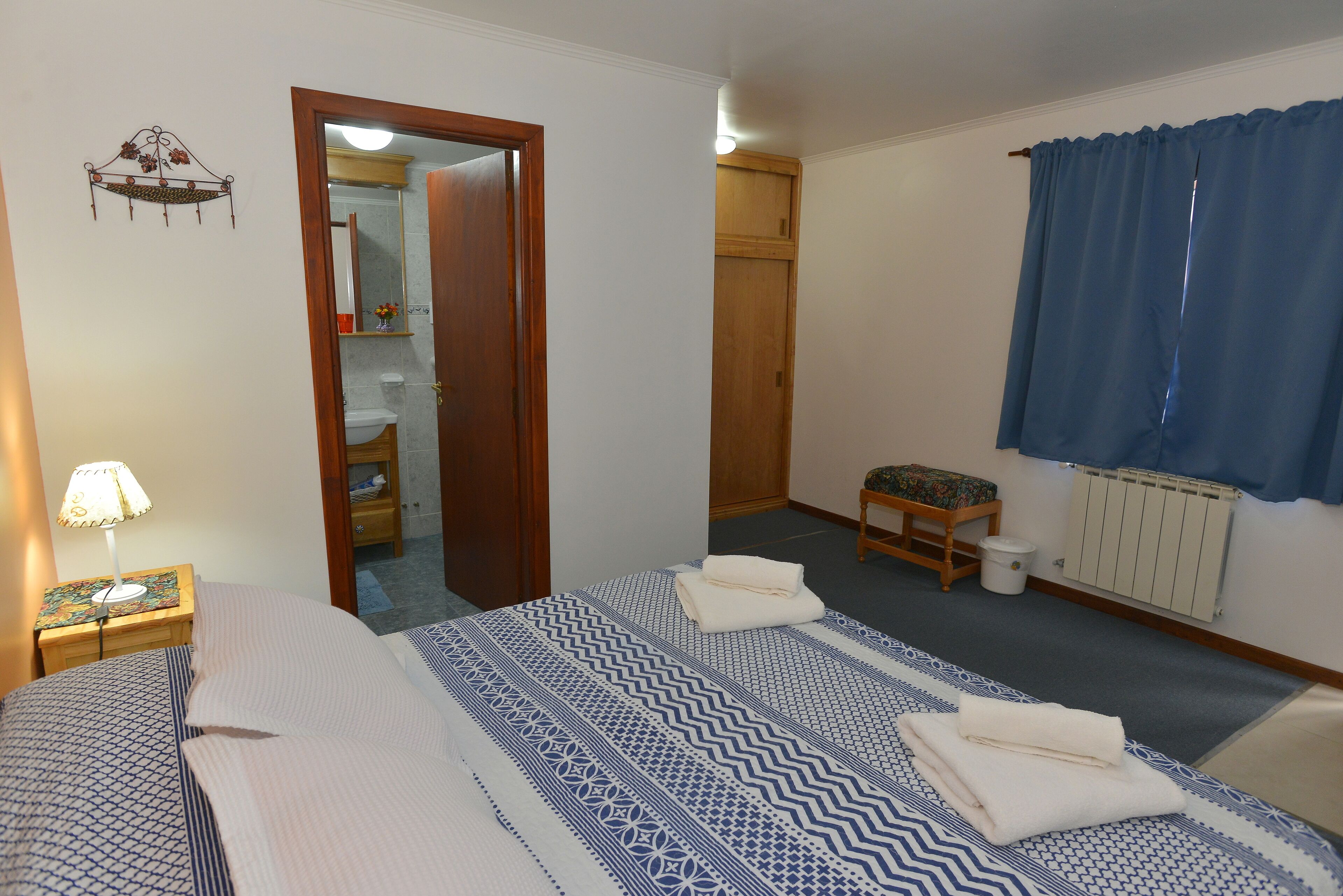 Ein Schlafzimmer mit Bett, Nachttisch, Holzschrank, einem kleinen Hocker und einer Heizung.