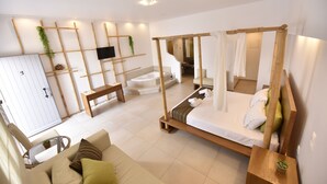 Un dormitorio moderno con cama con dosel, un sofá, un televisor y un baño al fondo.