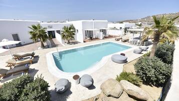 A pool area with lounge chairs and a small pool, surrounded by white buildings and palm trees.