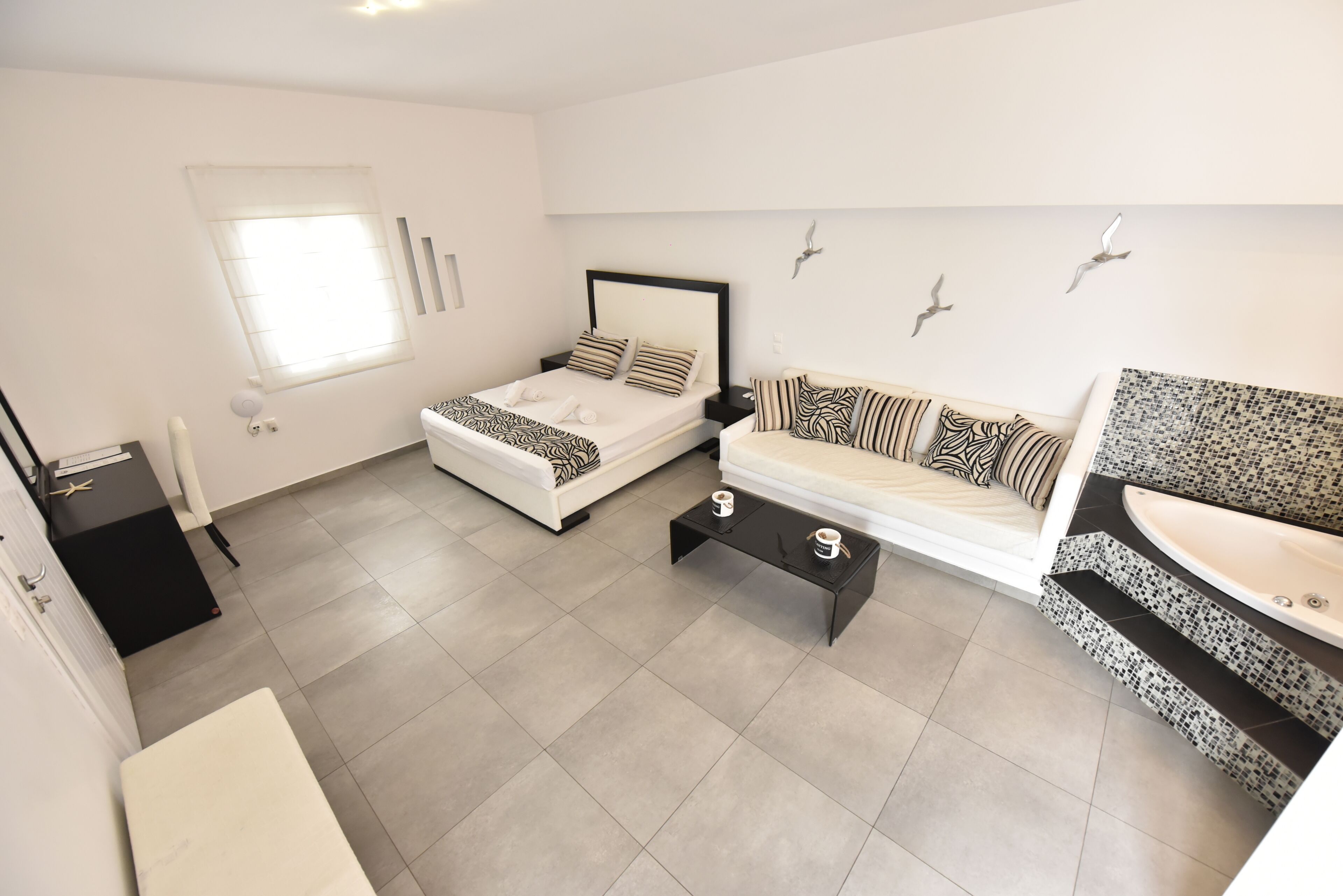 Una habitación de hotel moderna con una cama, un sofá, una mesita de centro y un baño con un lavamanos de mosaico.
