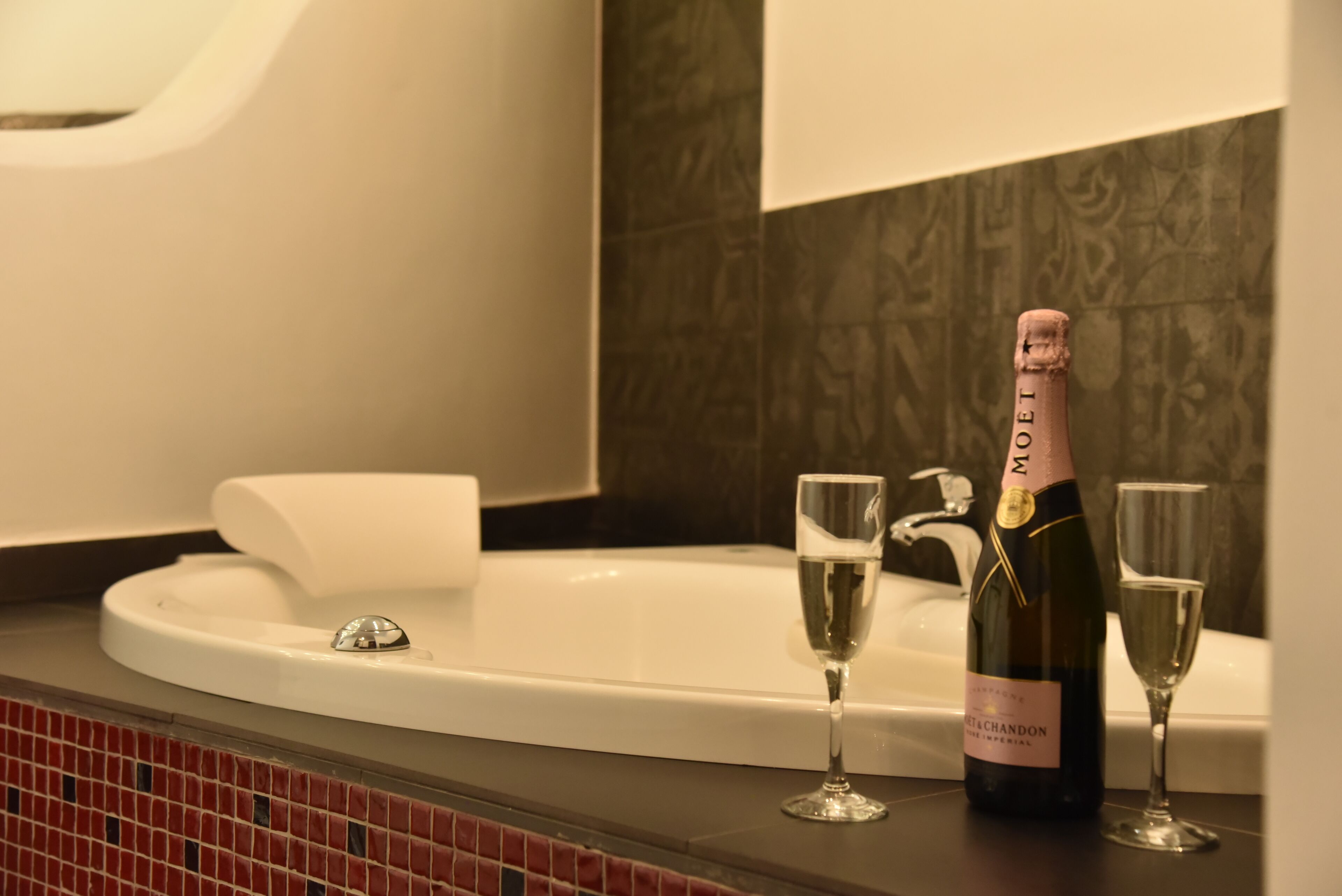 A bathroom with a white bathtub, two champagne glasses, and a bottle of champagne.