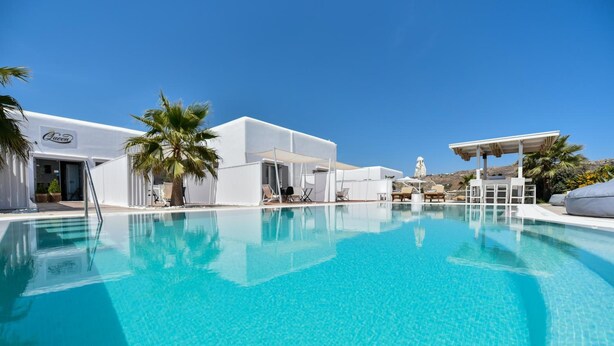 Una piscina con agua azul cristalina, rodeada de edificios blancos y palmeras.