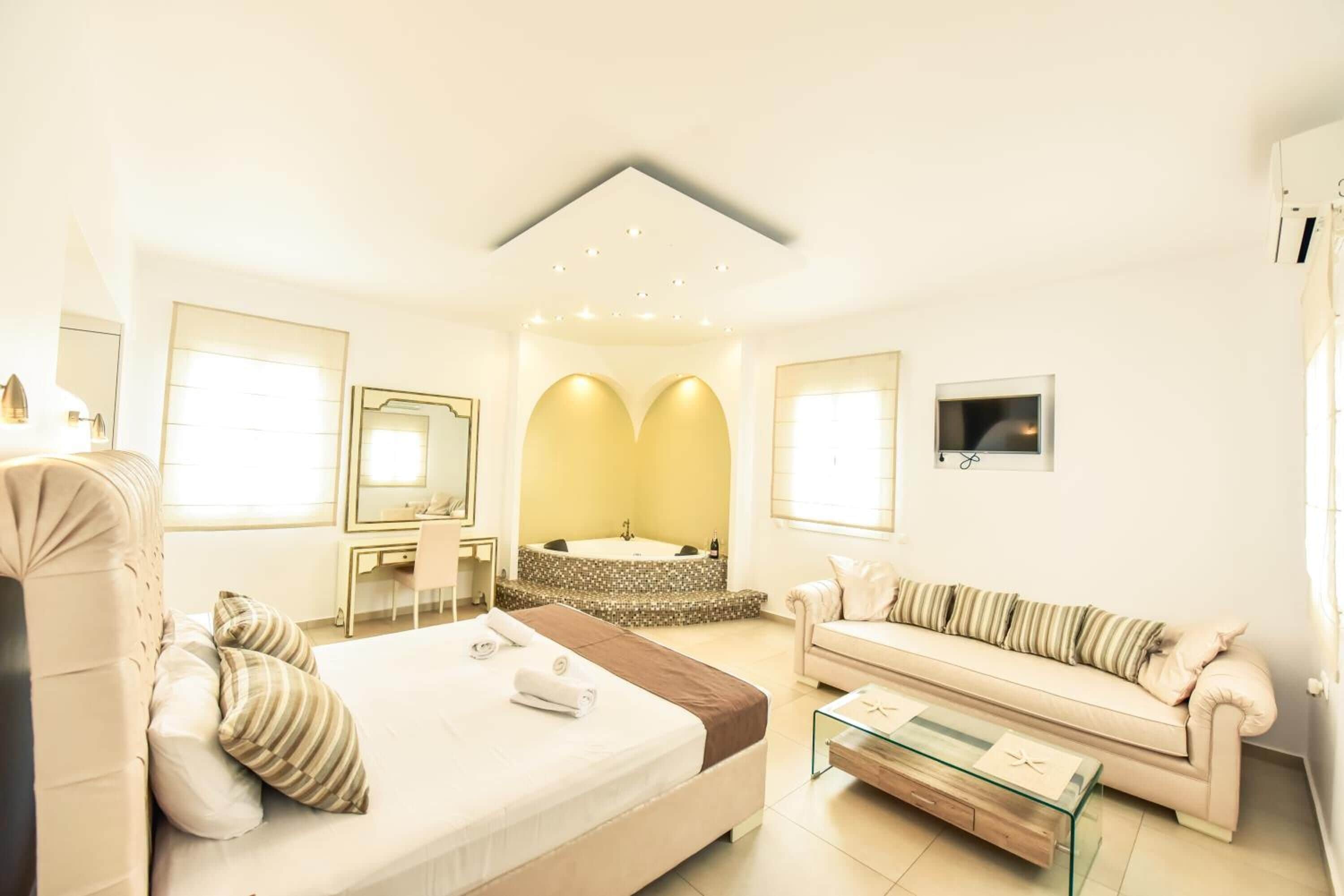 Una habitación de hotel moderna con una cama grande, un sofá, una mesa de centro de vidrio, un escritorio, un espejo y una bañera.
