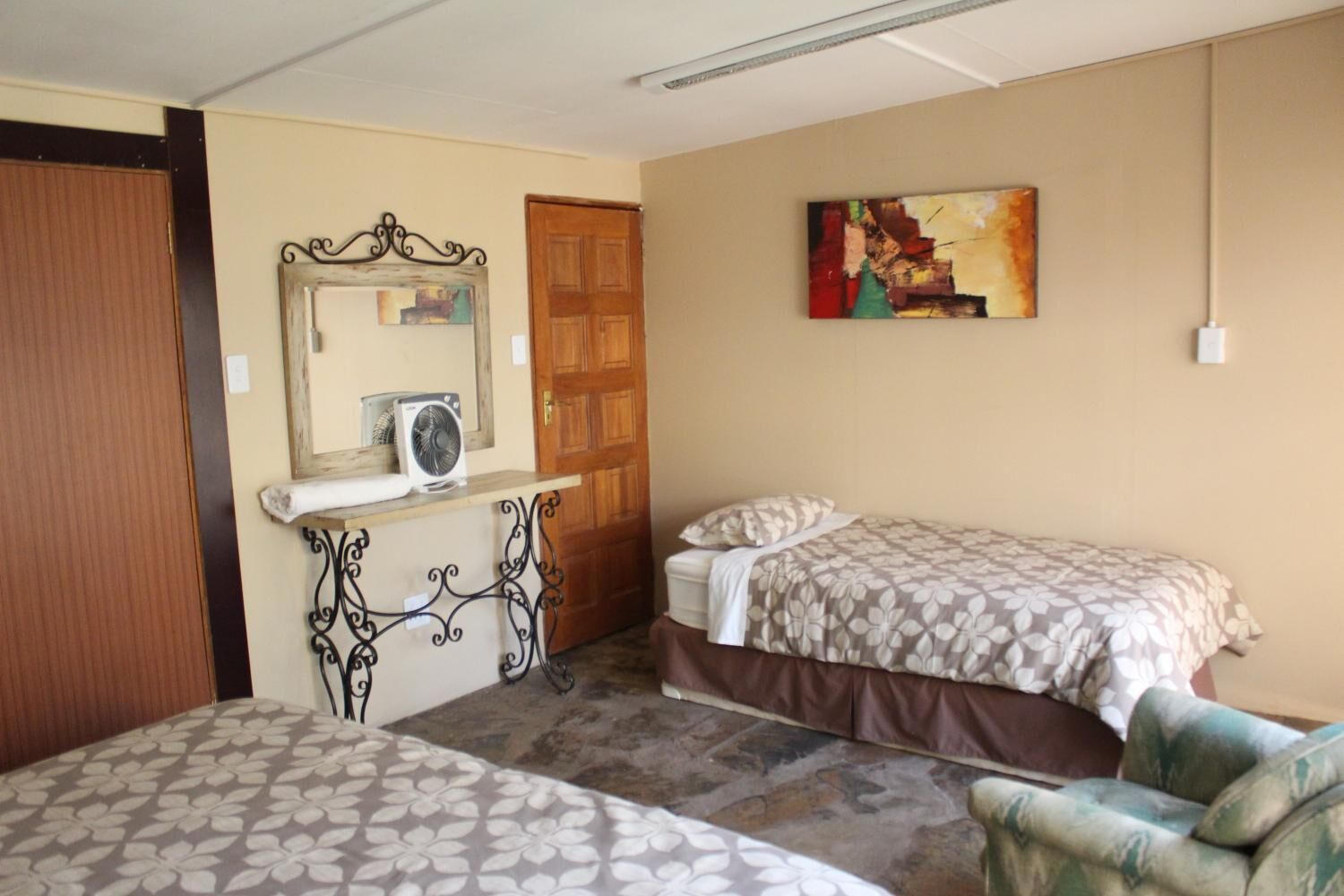 Una habitación con dos camas, una puerta de madera, un espejo, un ventilador y un cuadro en la pared.