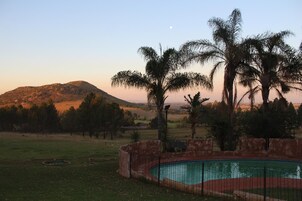 Una piscina rodeada por un muro de piedra, con palmeras y un paisaje montañoso al fondo.