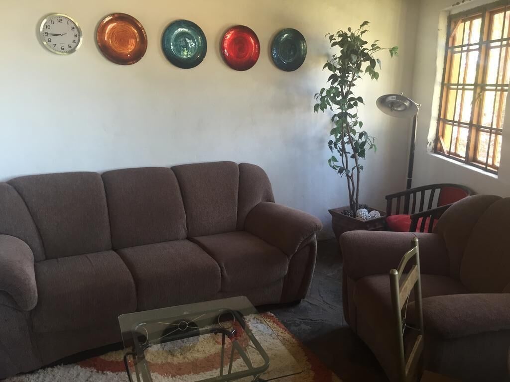 A living room with a brown sofa, a glass coffee table, a potted plant, and a window with a view.