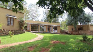 A building with a large glass facade, a stone wall, and a grassy lawn. - The Cradle Rest (Muldersdrift)