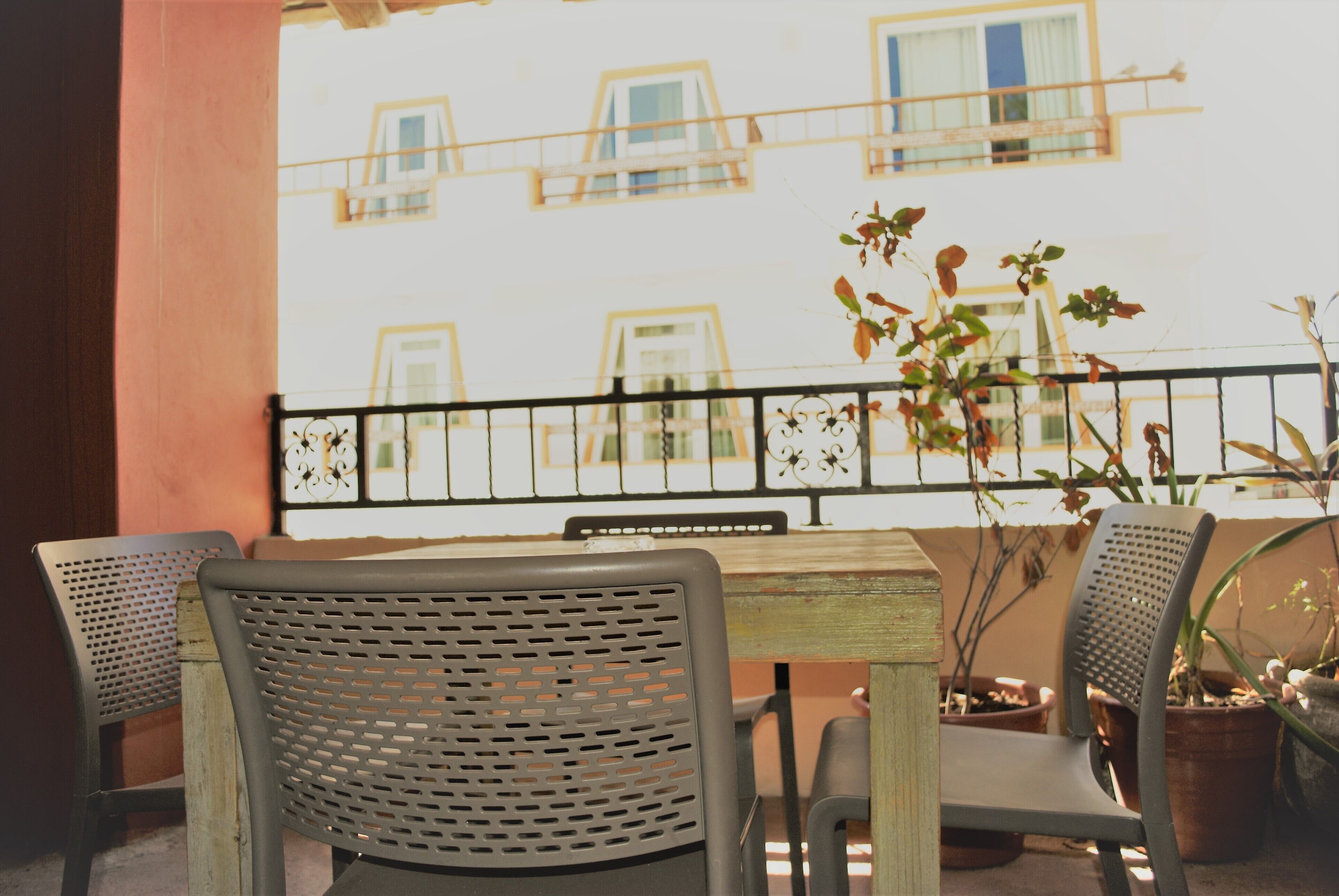 A balcony with a wooden table and two chairs, a railing, and potted plants.