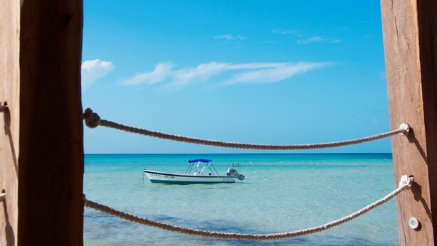 A wooden pier with a rope barrier, leading to clear turquoise waters where a boat is anchored. - Hotel Belmar (Isla Mujeres)
