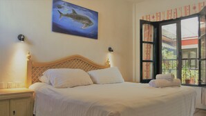 A bedroom with a bed, nightstands, a wall-mounted shark painting, and a window with curtains. - Hotel Belmar (Isla Mujeres)