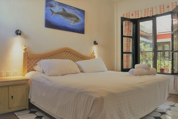 A bedroom with a bed, nightstands, a wall-mounted shark painting, and a window with curtains. - Hotel Belmar (Isla Mujeres)