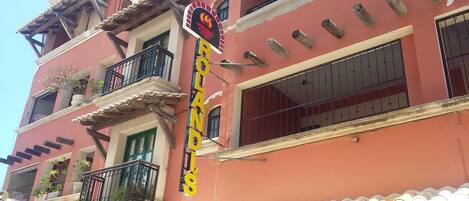 A building with a red facade, multiple balconies with black railings, and a sign with the name 'ROLAND'.