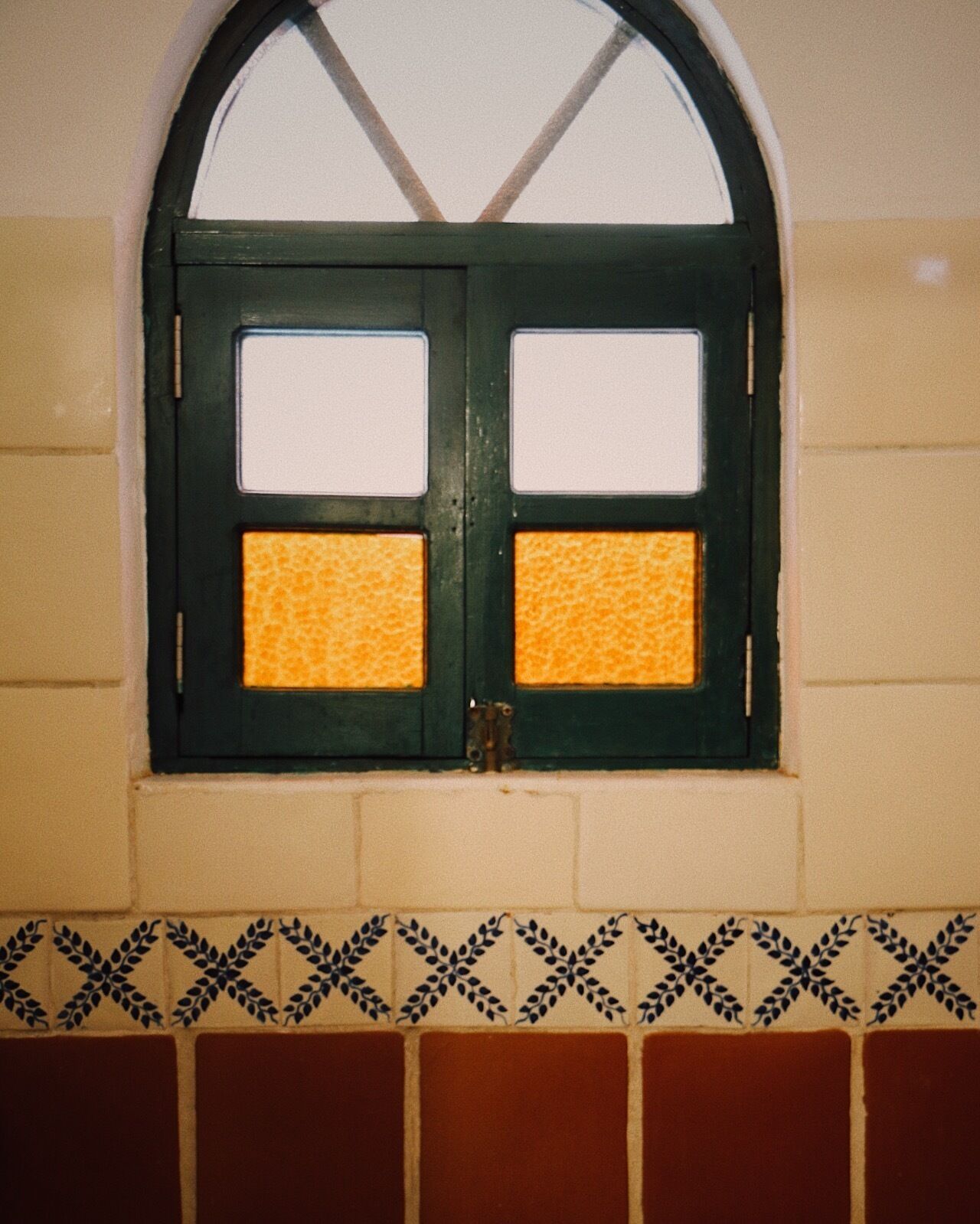 A window with a green frame and two glass panes, each with a yellow patterned section. Below the window, there is a decorative border with a leaf pattern.