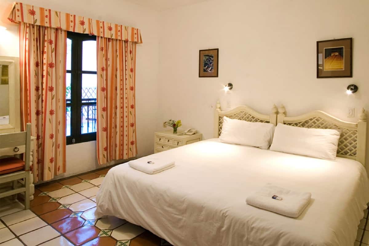A bedroom with a bed, a nightstand, a chair, a window with curtains, and two wall-mounted lights.