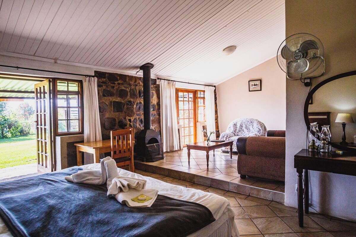 Ein gemütliches Zimmer mit einem Bett, einem Kamin aus Stein, einem Holztisch, einer Couch und einem Ventilator.