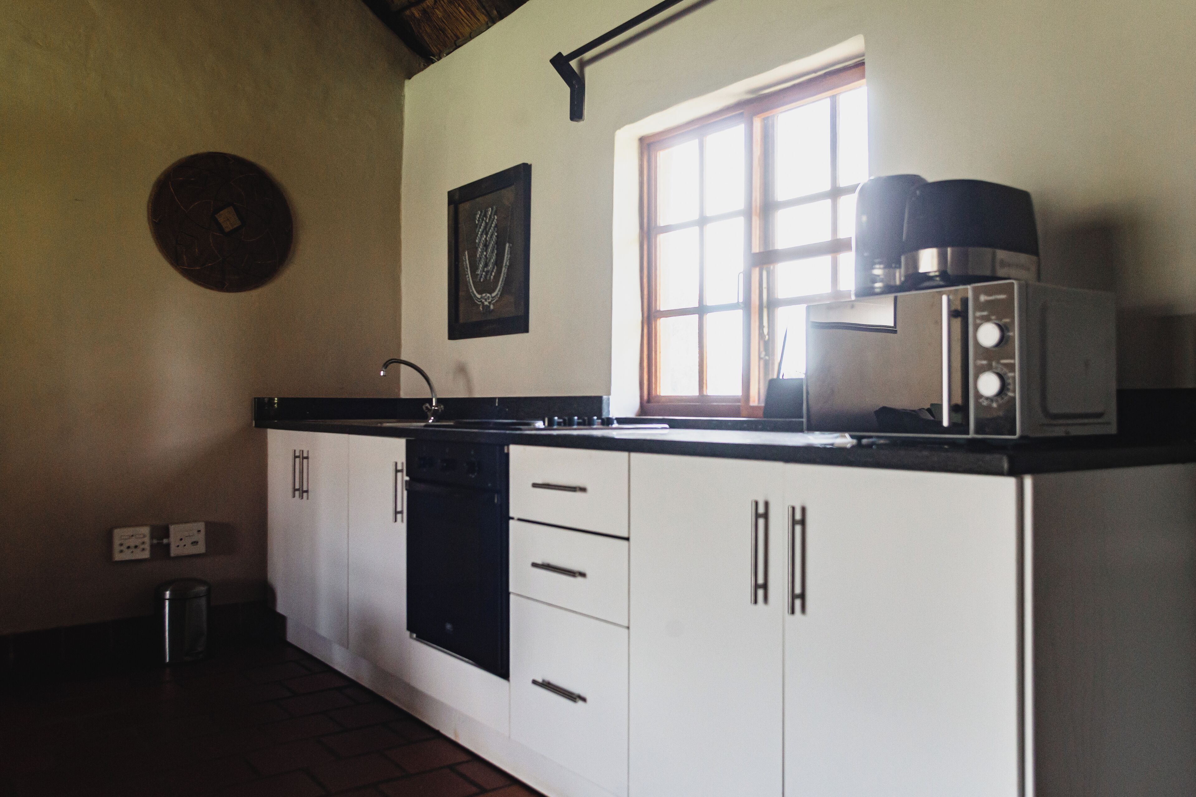 A kitchen with white cabinets, a black countertop, a window, and a coffee maker.