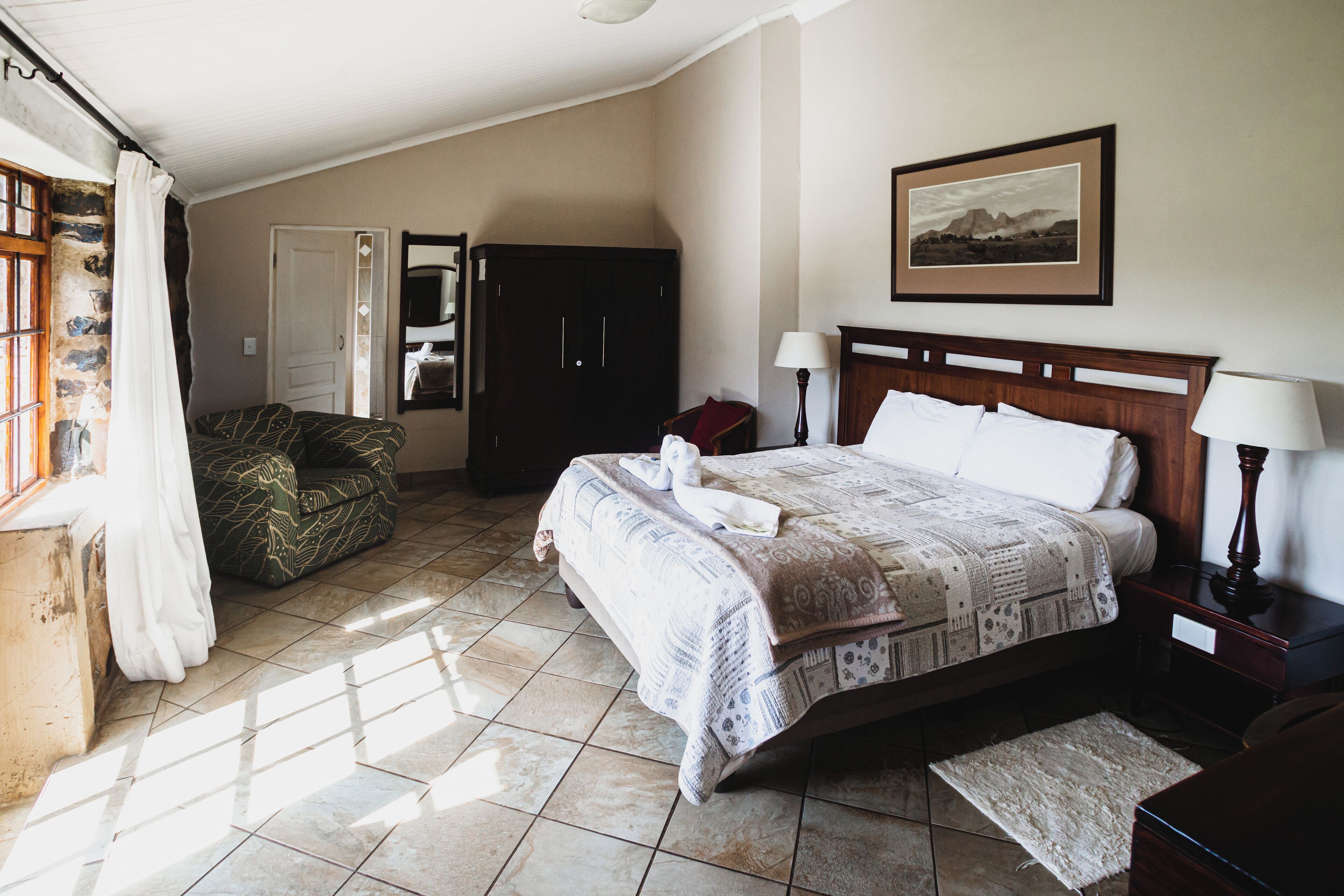 Quarto com cama, mesa de cabeceira, cômoda, cadeira e janela com cortinas.